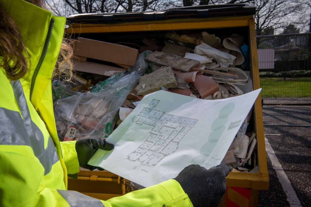 Operator inspecting site plan in front of full skip